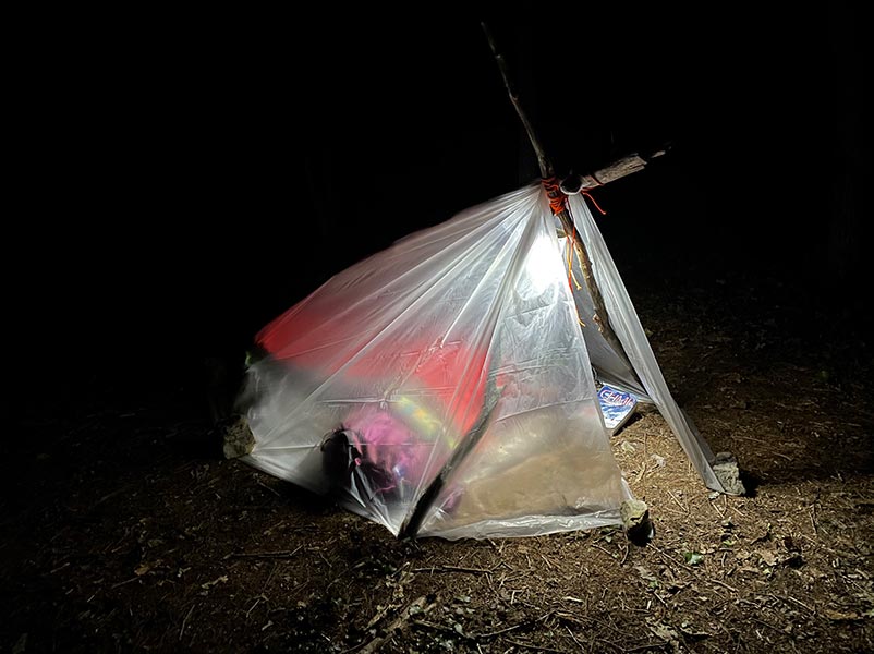 Makeshift A-frame shelter lit up at night.jpg